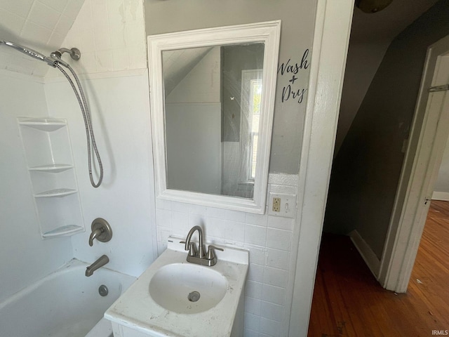 bathroom featuring vanity, tiled shower / bath combo, hardwood / wood-style flooring, tile walls, and vaulted ceiling