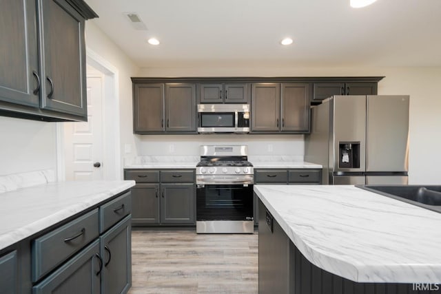 kitchen featuring stainless steel appliances, light stone countertops, a kitchen island, and light wood-type flooring