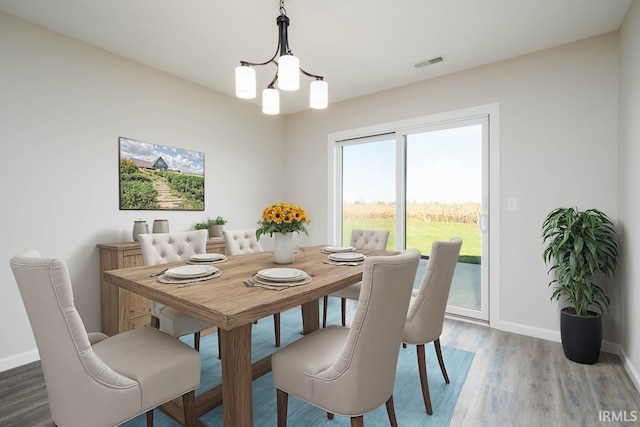dining space with baseboards, a notable chandelier, wood finished floors, and visible vents