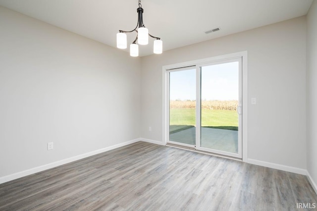 spare room featuring wood finished floors, visible vents, baseboards, and an inviting chandelier