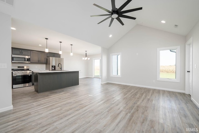 unfurnished living room featuring ceiling fan with notable chandelier, light wood-type flooring, high vaulted ceiling, and a wealth of natural light