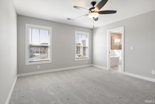 unfurnished bedroom with light colored carpet, connected bathroom, multiple windows, and ceiling fan