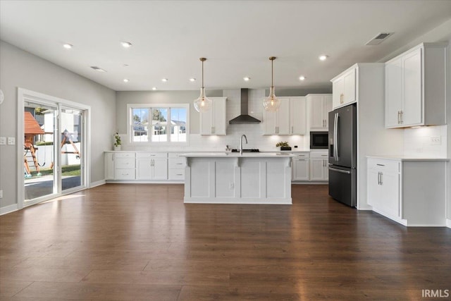 kitchen featuring stainless steel appliances, white cabinets, dark wood-type flooring, pendant lighting, and wall chimney range hood