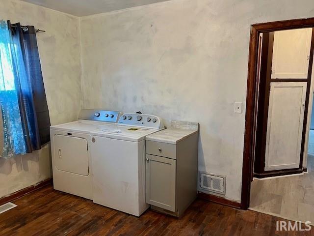 clothes washing area featuring washing machine and dryer, dark wood-type flooring, and cabinets