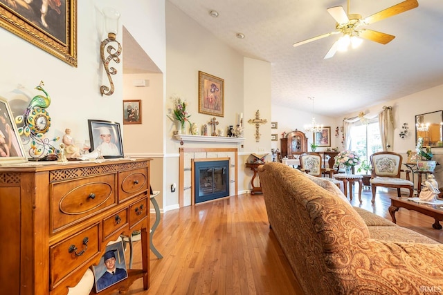 living room featuring ceiling fan with notable chandelier, light hardwood / wood-style flooring, a fireplace, lofted ceiling, and a textured ceiling