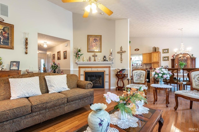 living room featuring a fireplace, ceiling fan with notable chandelier, high vaulted ceiling, and light hardwood / wood-style flooring