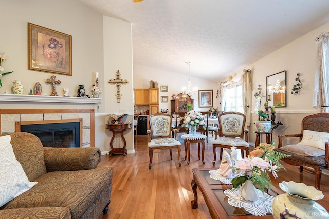 living room featuring light hardwood / wood-style floors, a chandelier, vaulted ceiling, and a tile fireplace