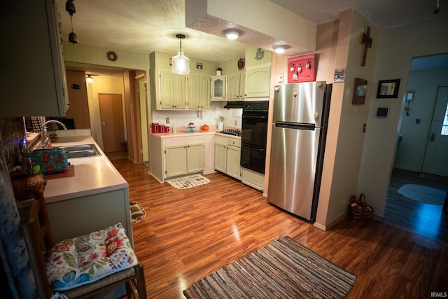 kitchen with stainless steel appliances, sink, pendant lighting, light hardwood / wood-style flooring, and backsplash