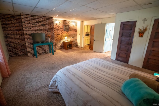 bedroom with carpet floors, a drop ceiling, and brick wall