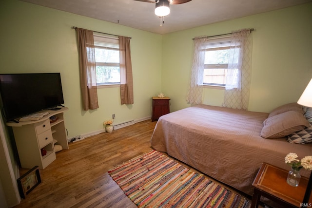 bedroom featuring wood-type flooring, a baseboard heating unit, multiple windows, and ceiling fan