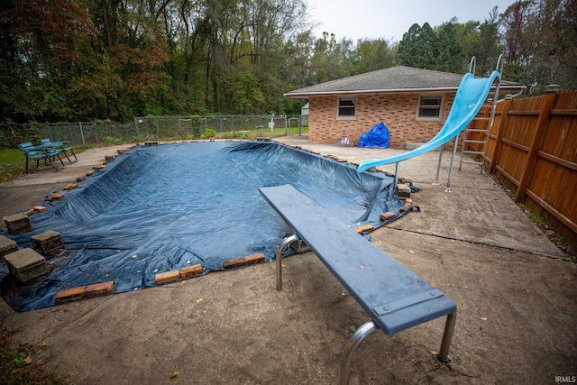 view of pool with a water slide, a diving board, and a patio area