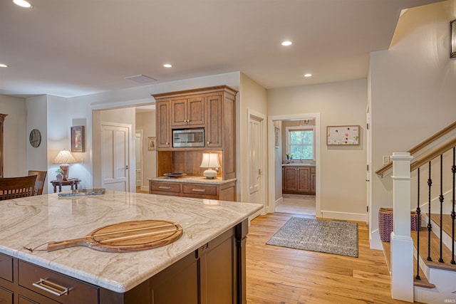 kitchen featuring stainless steel microwave, light stone countertops, light hardwood / wood-style flooring, and a center island