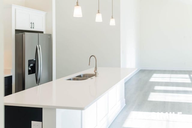 kitchen with hanging light fixtures, a kitchen island with sink, and stainless steel fridge