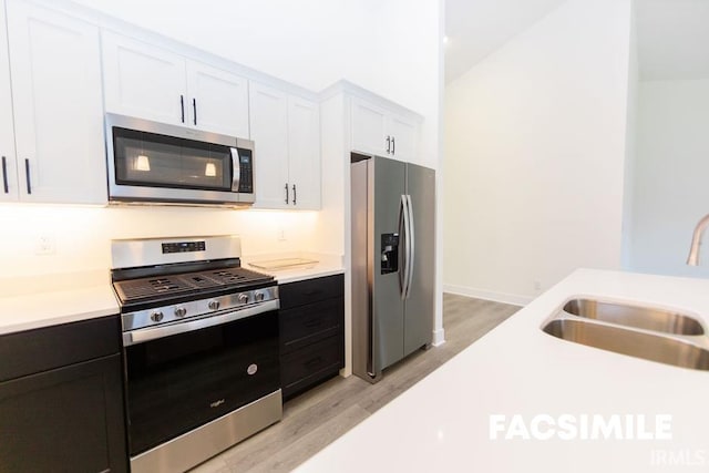 kitchen with stainless steel appliances, white cabinets, sink, vaulted ceiling, and light hardwood / wood-style flooring