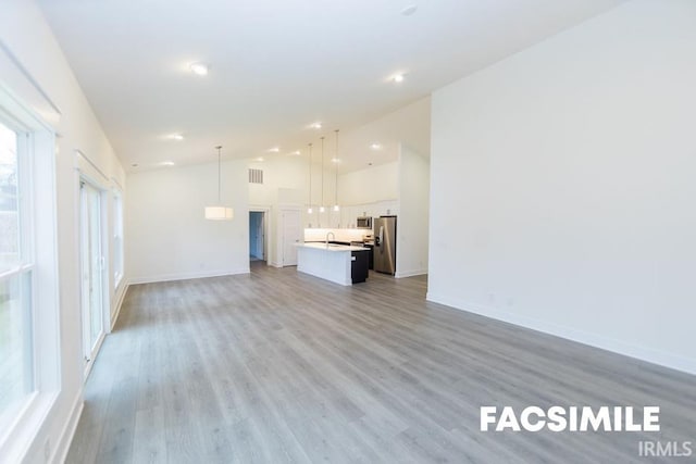 unfurnished living room with light wood-type flooring, sink, and lofted ceiling