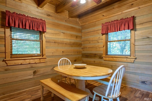 dining space with hardwood / wood-style flooring, wood walls, and beam ceiling