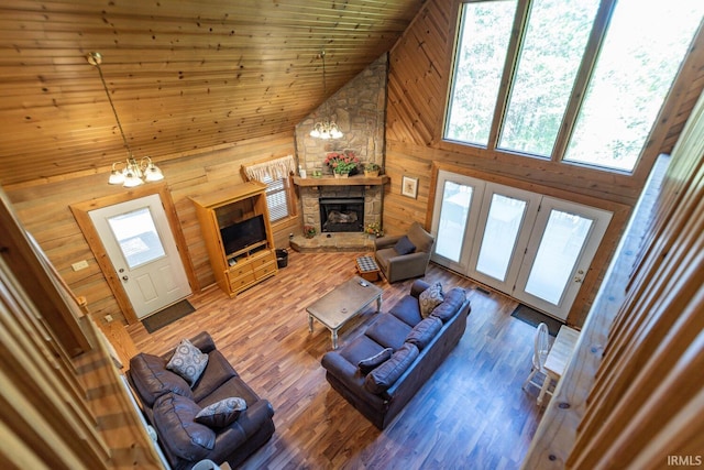 living room featuring hardwood / wood-style floors, a notable chandelier, wooden walls, a fireplace, and high vaulted ceiling