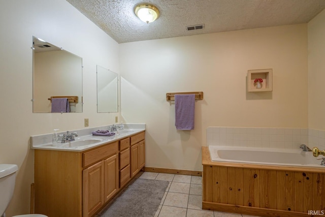 bathroom featuring a tub to relax in, vanity, tile patterned floors, toilet, and a textured ceiling