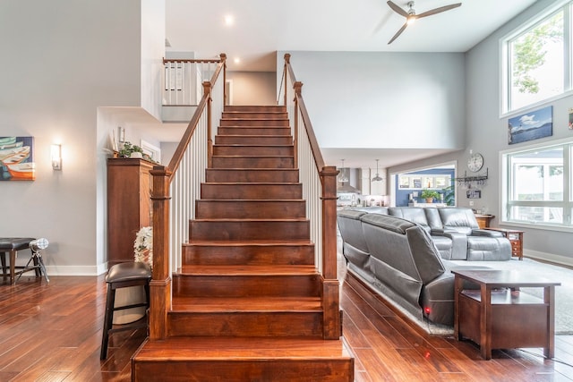 staircase featuring a high ceiling, a healthy amount of sunlight, ceiling fan, and hardwood / wood-style floors