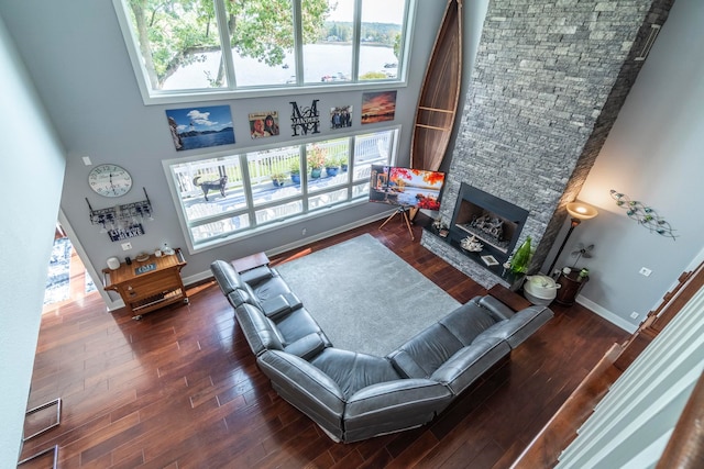 living room with dark wood-type flooring, a towering ceiling, and a stone fireplace