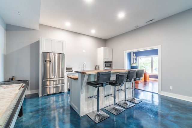 kitchen featuring a breakfast bar, white cabinetry, stainless steel appliances, a center island, and wood counters