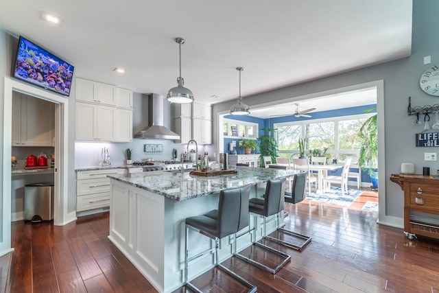 kitchen with a kitchen island with sink, wall chimney exhaust hood, dark hardwood / wood-style flooring, and white cabinetry