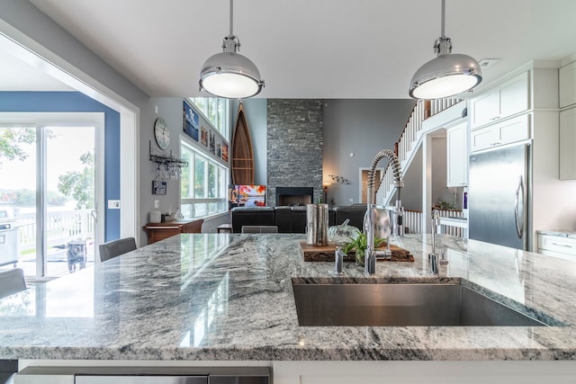 kitchen featuring a stone fireplace, stainless steel built in refrigerator, hanging light fixtures, and sink