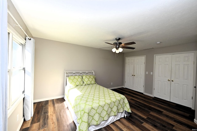 bedroom with ceiling fan, dark wood-type flooring, and two closets