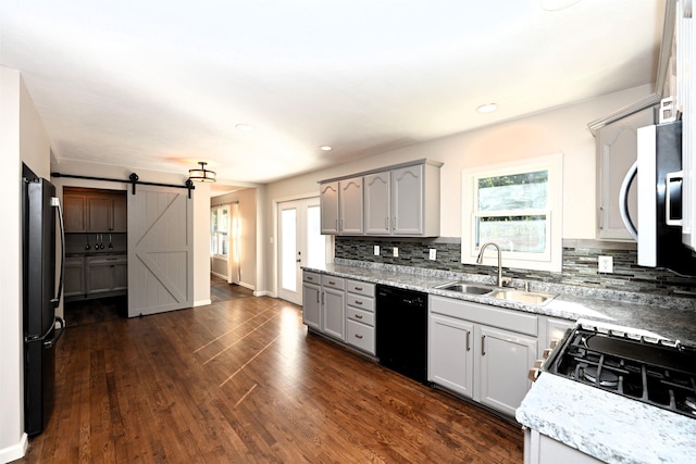 kitchen with sink, plenty of natural light, appliances with stainless steel finishes, a barn door, and dark hardwood / wood-style flooring