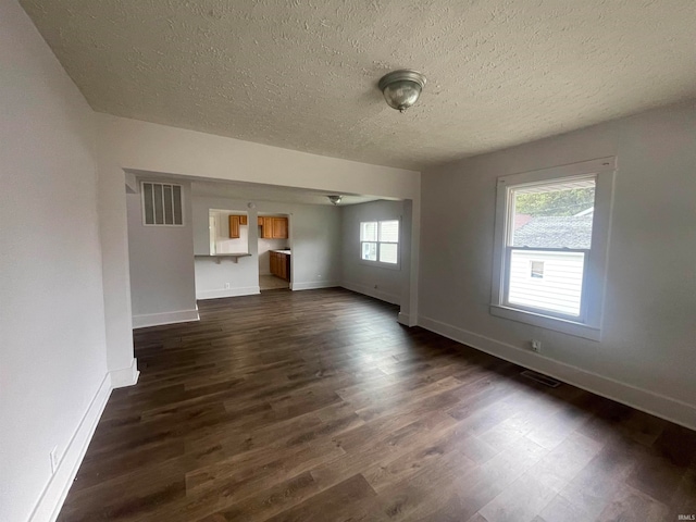 unfurnished living room with plenty of natural light, dark hardwood / wood-style floors, and a textured ceiling