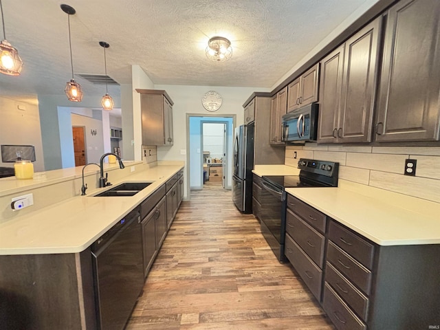 kitchen with dark brown cabinetry, hanging light fixtures, a textured ceiling, light hardwood / wood-style flooring, and black appliances