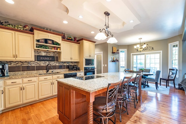 kitchen with tasteful backsplash, light hardwood / wood-style flooring, a center island with sink, black appliances, and a breakfast bar area