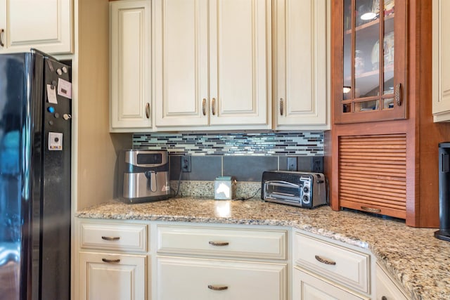 kitchen with backsplash, white cabinets, and black refrigerator