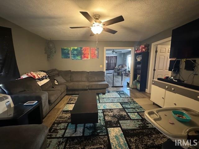 living room featuring ceiling fan, light hardwood / wood-style flooring, and a textured ceiling