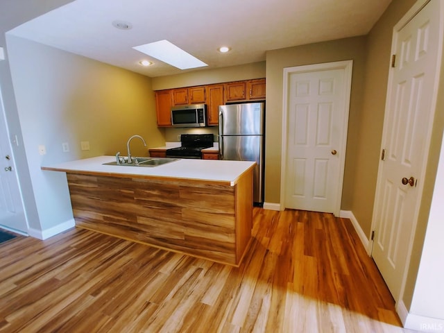 kitchen featuring sink, a skylight, kitchen peninsula, light hardwood / wood-style flooring, and appliances with stainless steel finishes