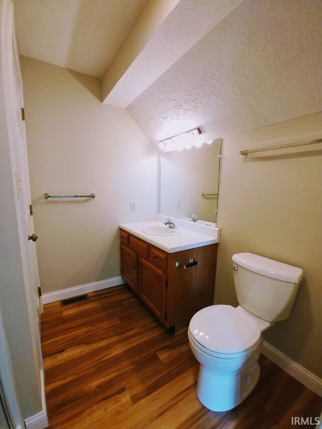 bathroom with toilet, wood-type flooring, vaulted ceiling, vanity, and a textured ceiling