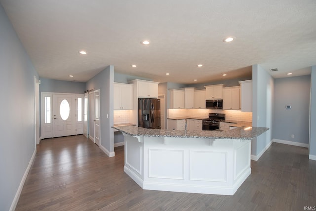 kitchen with appliances with stainless steel finishes, light stone countertops, dark hardwood / wood-style floors, and white cabinets