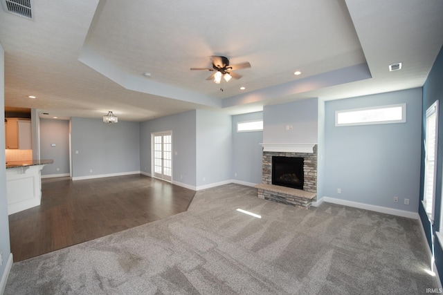 unfurnished living room featuring ceiling fan with notable chandelier, a fireplace, plenty of natural light, and dark wood-type flooring