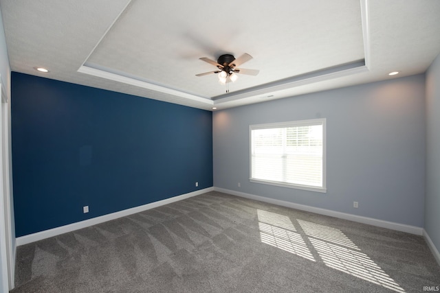 empty room with ceiling fan, carpet floors, and a raised ceiling