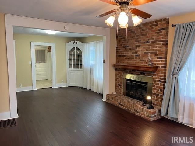 unfurnished living room featuring ceiling fan, a brick fireplace, and dark wood-type flooring