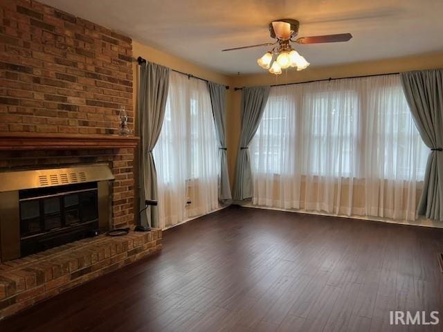 unfurnished living room with a brick fireplace, plenty of natural light, and dark wood-type flooring