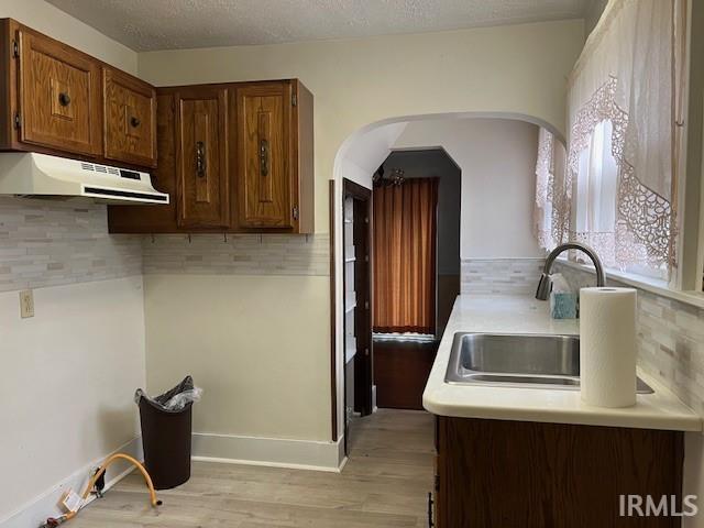 kitchen featuring a textured ceiling, decorative backsplash, sink, and light hardwood / wood-style flooring