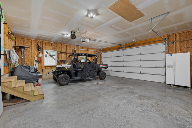 garage with a garage door opener and white refrigerator with ice dispenser