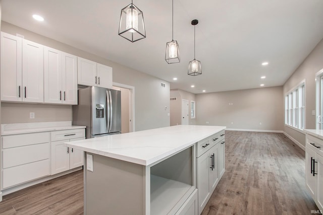 kitchen with stainless steel fridge, light wood-type flooring, a kitchen island, hanging light fixtures, and white cabinets