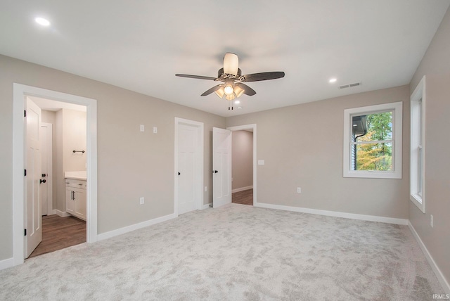 unfurnished bedroom with light colored carpet, ensuite bathroom, and ceiling fan