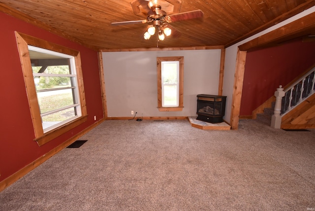 unfurnished living room featuring carpet floors, ceiling fan, wood ceiling, and a wood stove