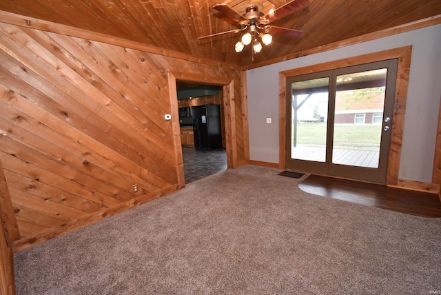 spare room featuring wooden ceiling, dark colored carpet, wooden walls, and ceiling fan