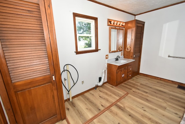 washroom featuring light hardwood / wood-style floors, sink, ornamental molding, and a textured ceiling