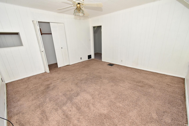 unfurnished bedroom with carpet floors, wood walls, and ceiling fan