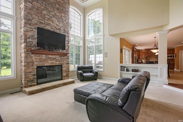 carpeted living room with a stone fireplace, crown molding, a high ceiling, and a healthy amount of sunlight